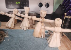 Four handmade corn husk dolls lined up on a towel after a family Mabon craft.