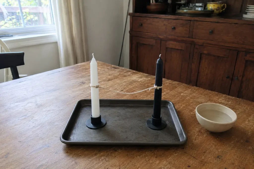 Black and white chime candles connected with cotton string on a fire-safe tray