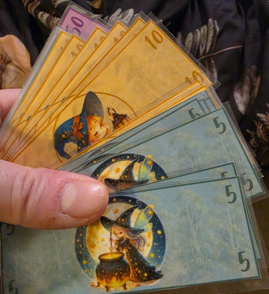 Laminated Witch Bucks printable play money in several denominations held in one hand